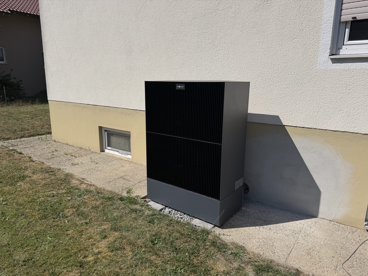 Modernes Wärmepumpen-Außengerät neben einem Wohngebäude